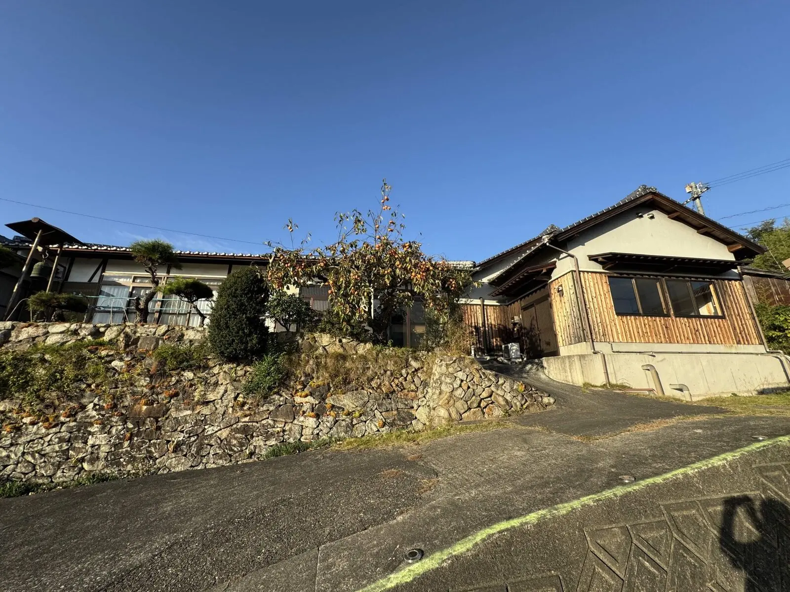 La maison KANAYA vue depuis la rue — toit de tuiles, façade en bois, muret de pierres